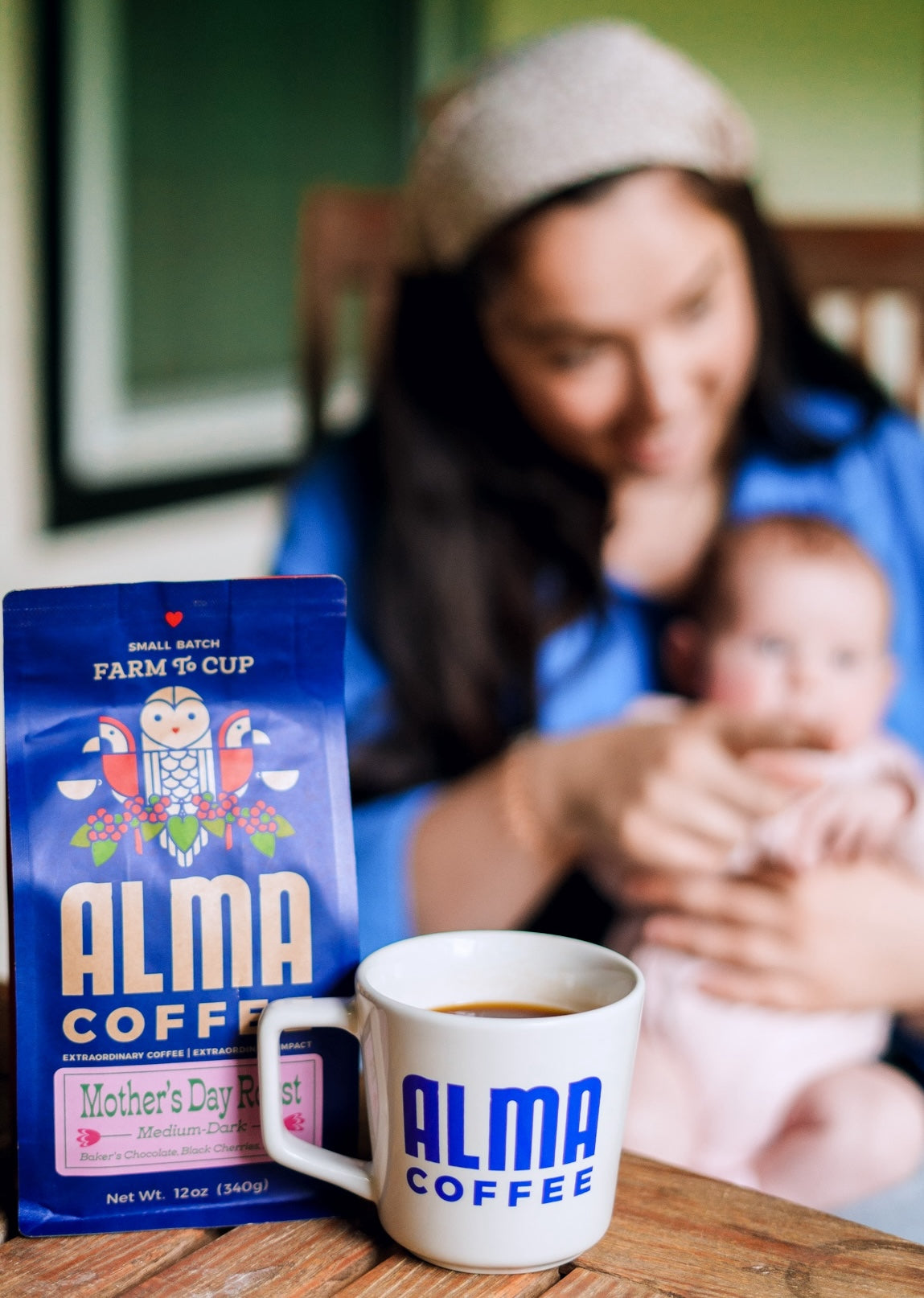 Mom holding her baby with Alma Coffee Mother's Day Roast in the Foreground